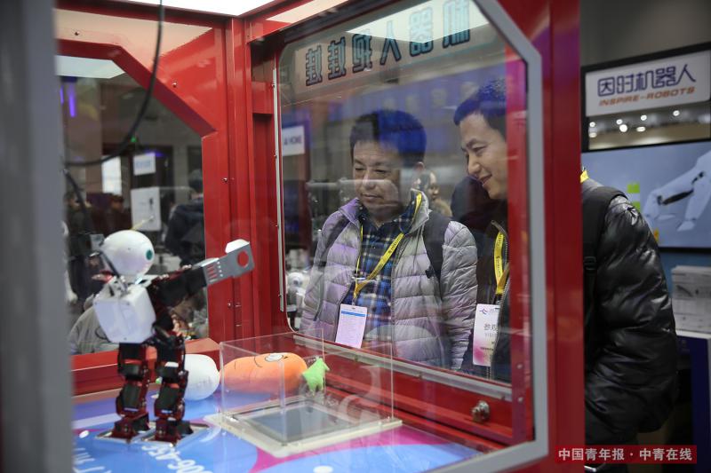 12月8日，两位参观者观看“机器人抱娃娃”的表演。通过程序输入，该款机器人可以按照人的指令将玩具娃娃投入出口。段经琨/摄