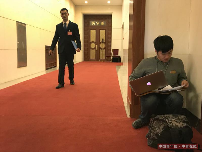 3月15日上午，全国政协十三届一次会议闭幕会后，中国青年报·中青在线记者卢义杰在清场间隙蹲在大会堂角落向后方传回稿件。 中国青年报·中青在线记者 章正/摄
