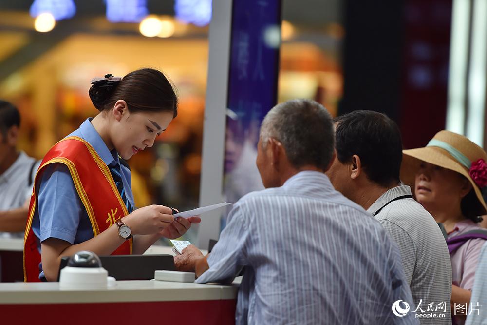 2017年8月21日，北京站服务台工作人员正在为旅客耐心解答问题。当日起铁路部门迎来暑运返程客流高峰。（人民网记者 翁奇羽 摄）