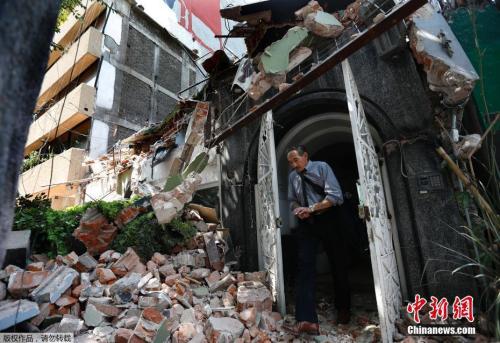 墨西哥城Condesa区，一名男士从楼房里出来，门外是满地的房屋瓦砾，建筑已成废墟。