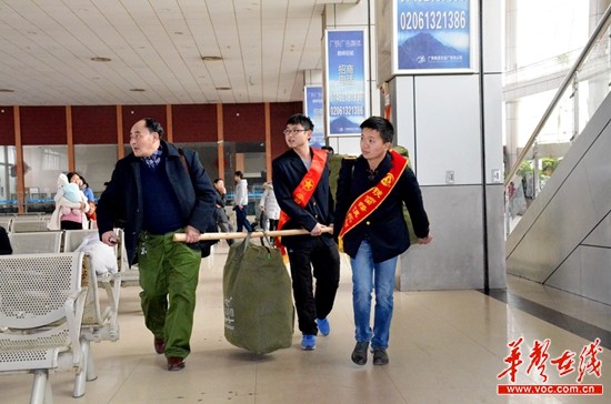 龙伟华和其他志愿者一起帮助旅客扛、挑大件行李。